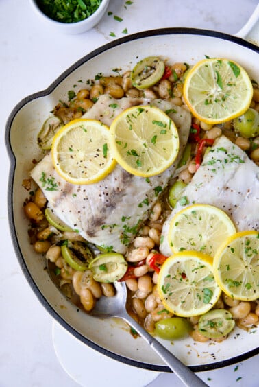 Mediterranean Fish and White Bean Skillet in white cast iron skillet topped with lemon slices.