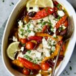 Greek Baked Chicken in white oval baking dish with serving fork.