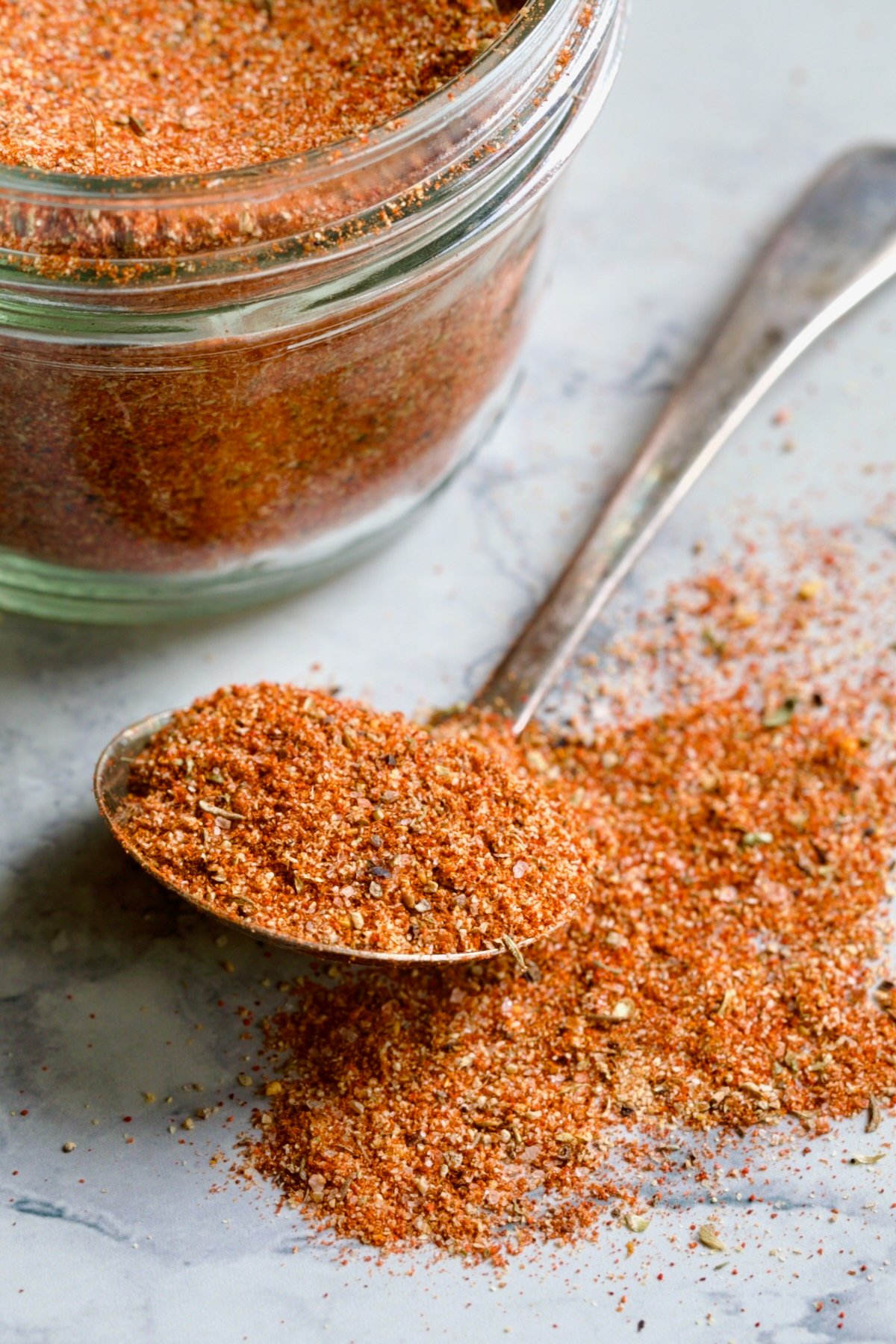 Spoon of Blackening Seasoning spilling over onto surface with jar in the background.