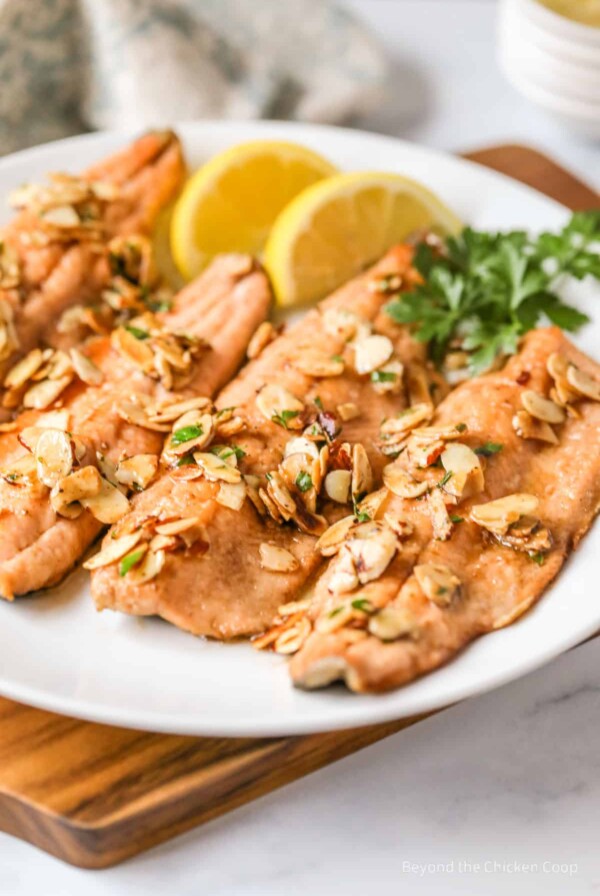 Trout Almondine on white plate with lemon wedges.