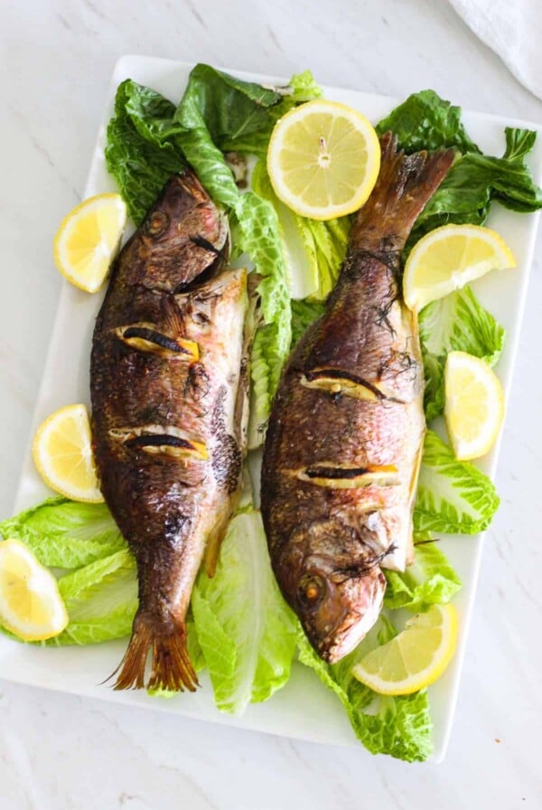Two baked whole red snapper on platter.
