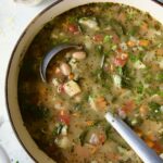Finished soup in white Dutch oven with soup ladle.