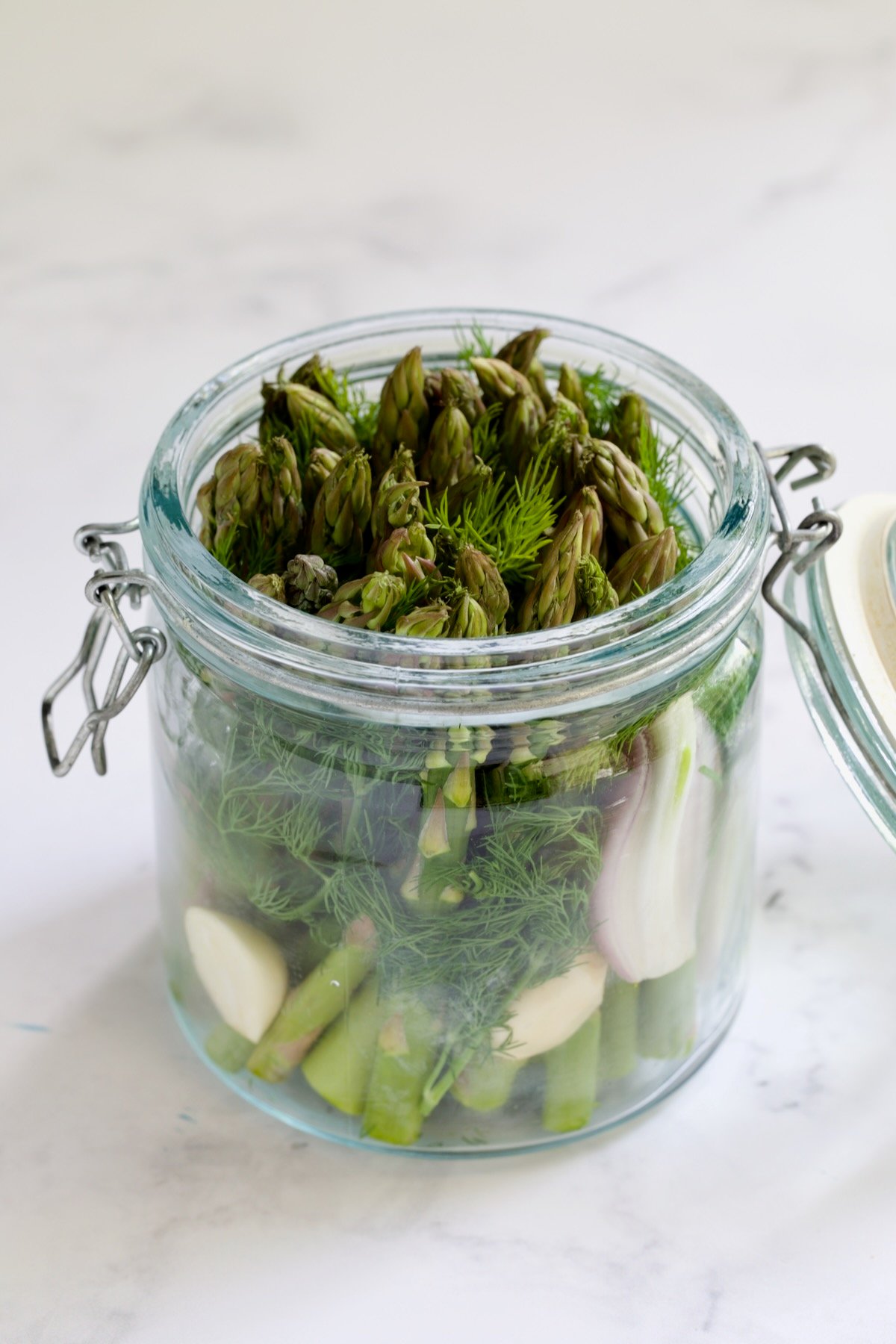 Asparagus, fresh dill, shallot and garlic in glass jar before brine is poured over.