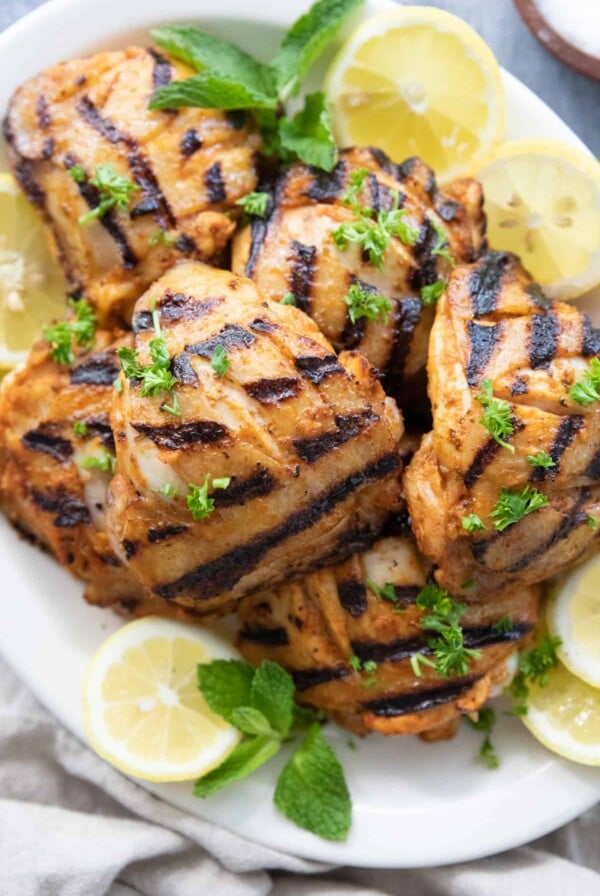 Platter full of Harissa Grilled Chicken Thighs garnished with lemon wedges.