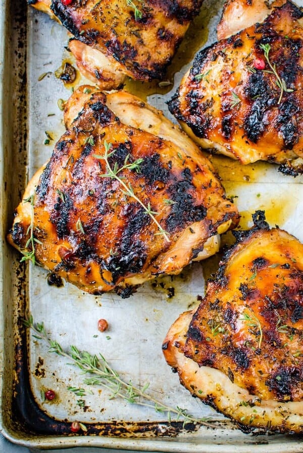 Four herb-rubbed chicken thighs on parchment paper lined baking sheet.