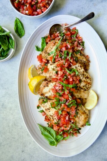 Chicken Bruschetta on oval white platter garnished with fresh lemons and basil.
