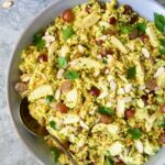 Chicken Couscous Salad in gray bowl with serving spoon with bowl of sliced almonds, whole grapes and lemon wedges.