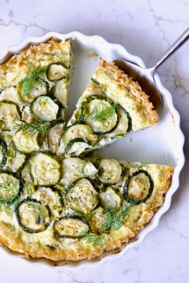 Zucchini Quiche in white quiche dish with pie server picking up a piece.