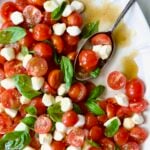 Caprese Salad with Cherry Tomatoes on white oval platter with serving spoon.