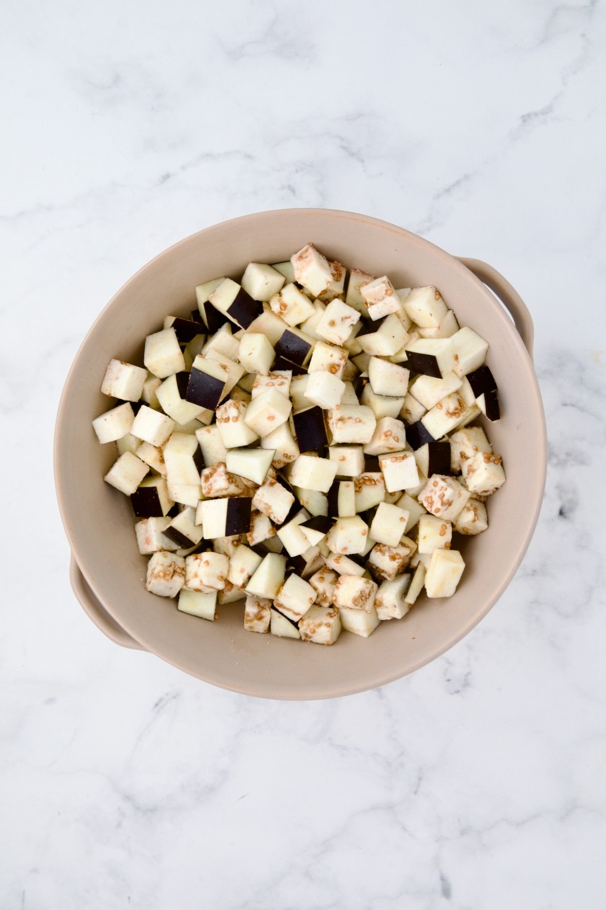 Cubes of eggplant in beige colander.