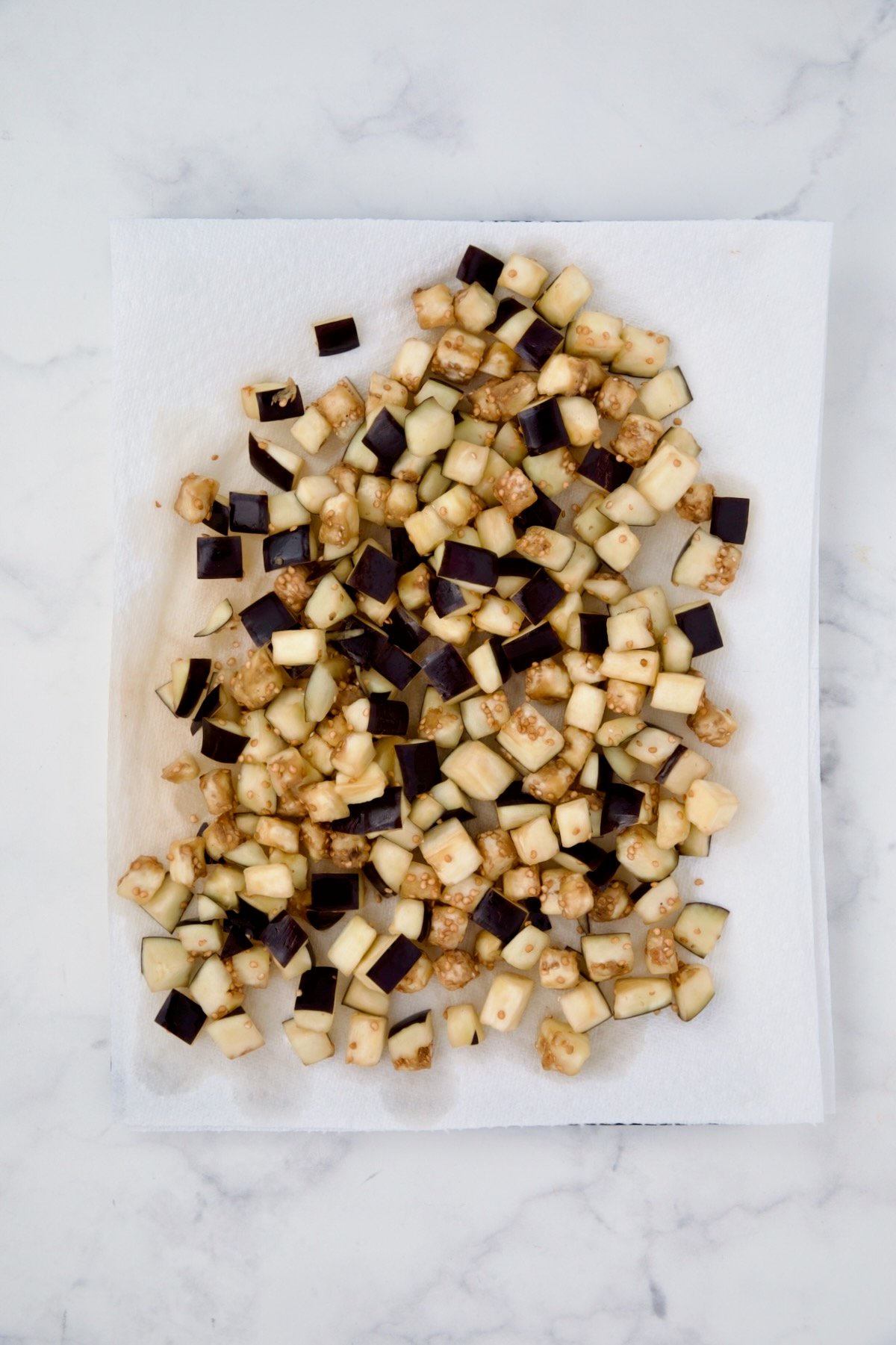 Cubes of eggplant on paper towels being dabbed dry.