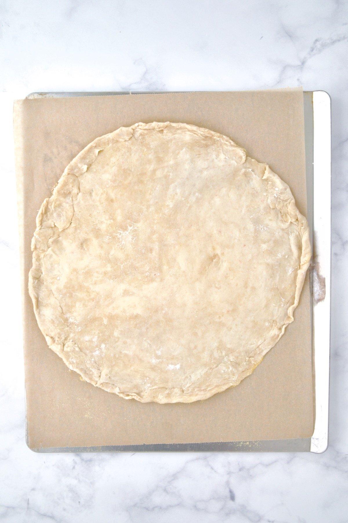 Rolled out galette dough on parchment paper on cookie sheet.