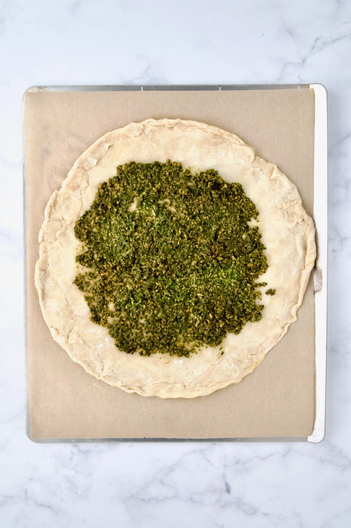 Rolled out galette dough on parchment paper on cookie sheet with pesto added.