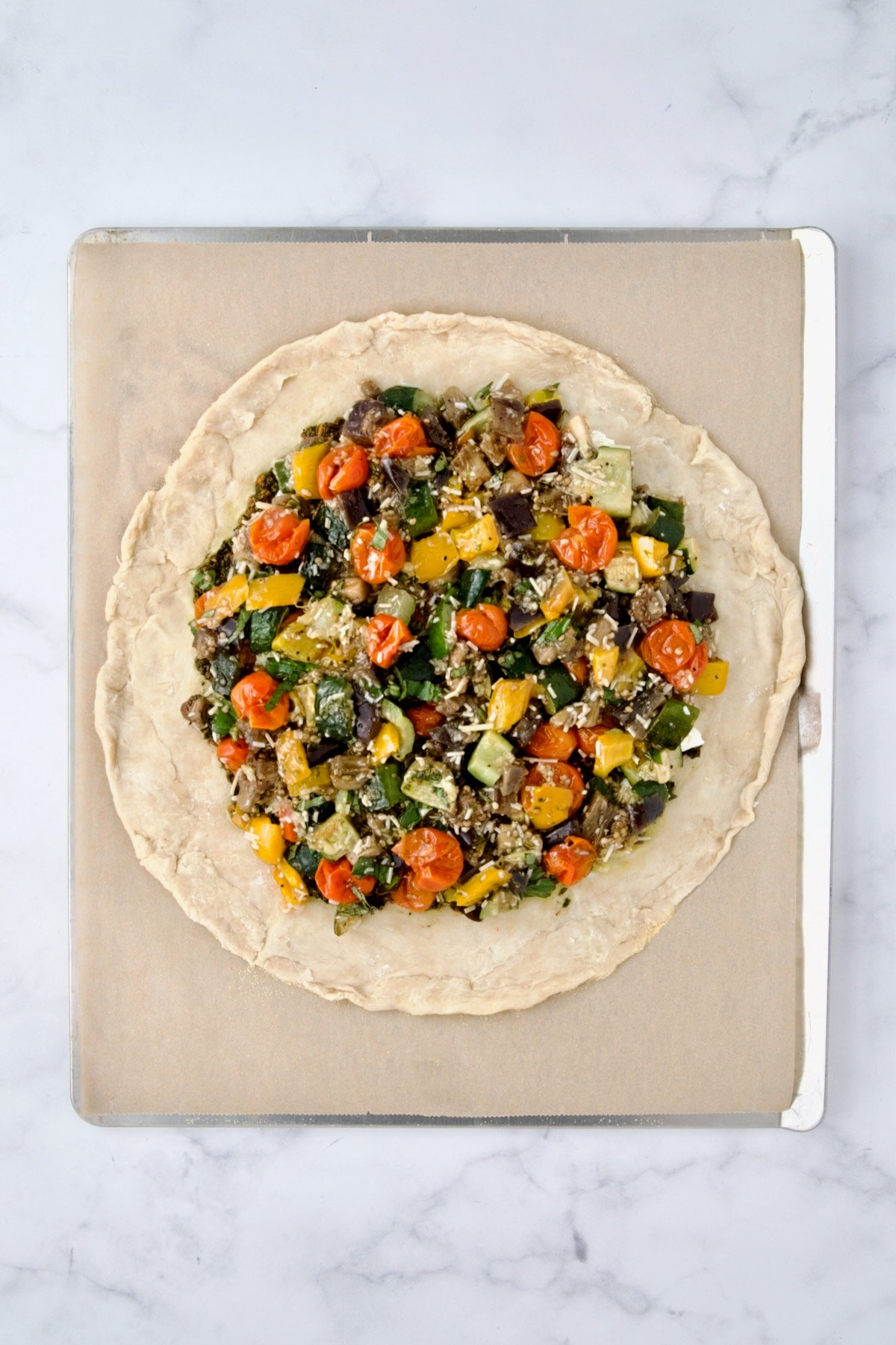 Roasted vegetables added to pesto and goat cheese on rolled out galette dough on parchment paper lined cookie sheet.