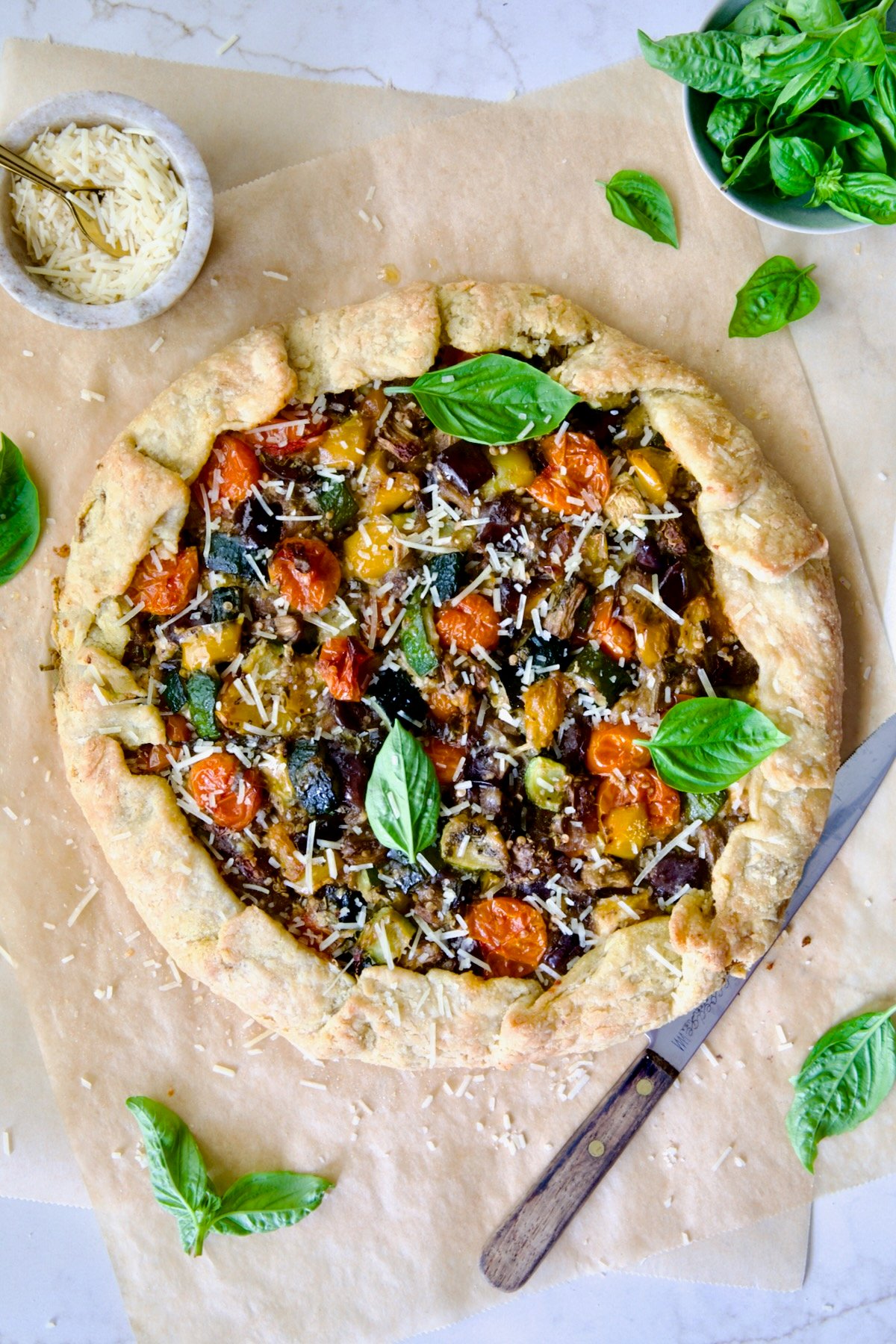 Baked Mediterranean Vegetable Galette on parchment paper garnished with fresh basil and sprinkled with Parmesan cheese.