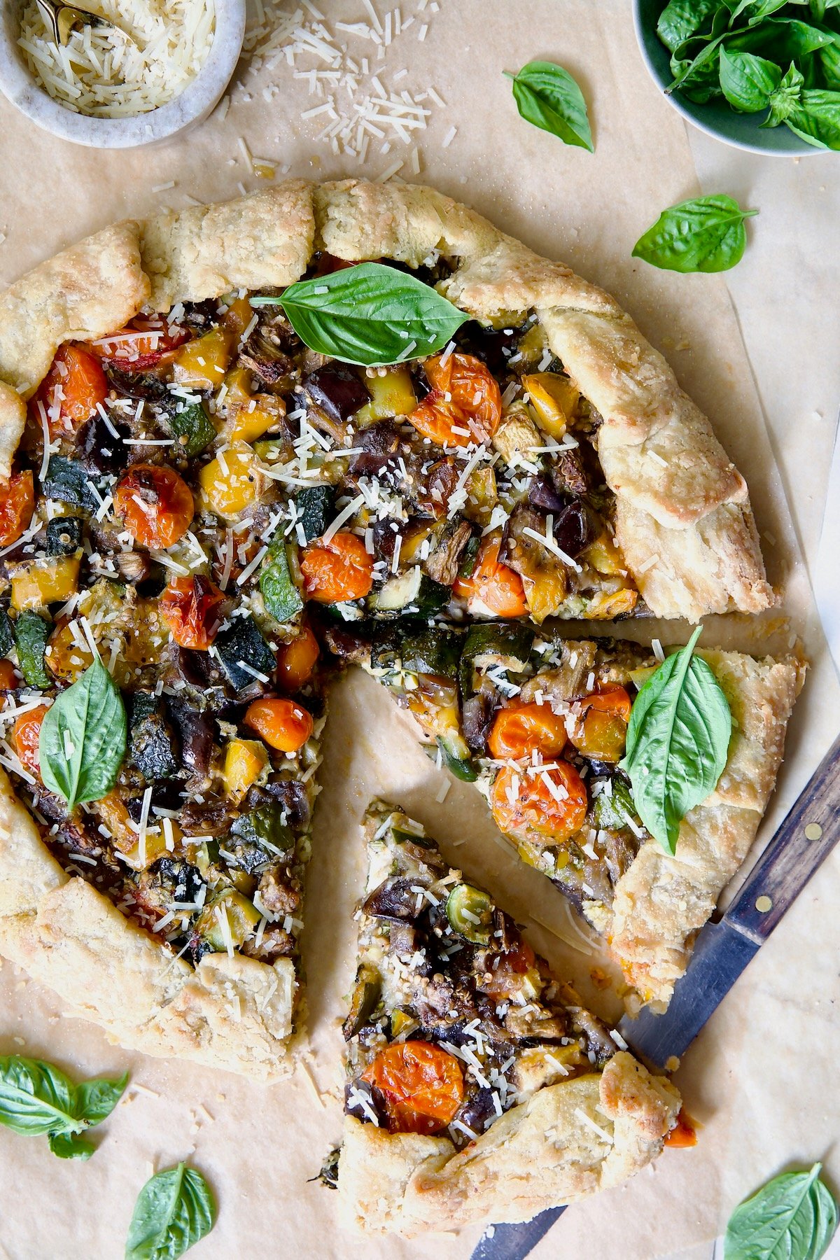 Mediterranean Vegetable Galette on parchment paper garnished with fresh basil with two wedges cut.
