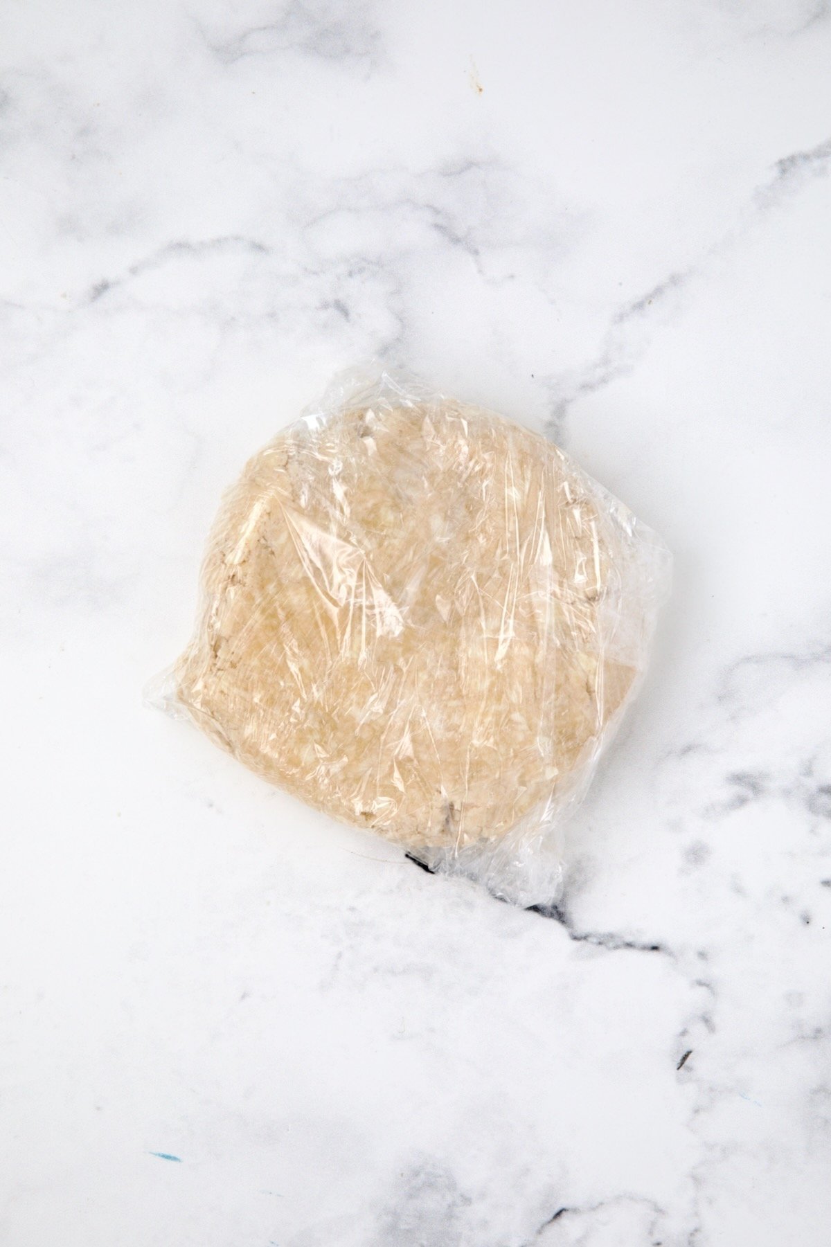 Dough for galette formed into a ball and wrapped with plastic.
