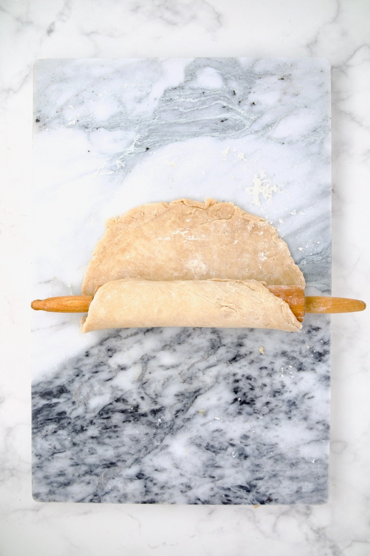 Galette dough on pastry board being rolled onto a rolling pin.