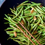 Thai Sweet Chili Green Beans in wok being stirred with wooden tongs.