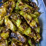 Blistered Shishito Peppers on blue oval platter garnished with sesame seeds.