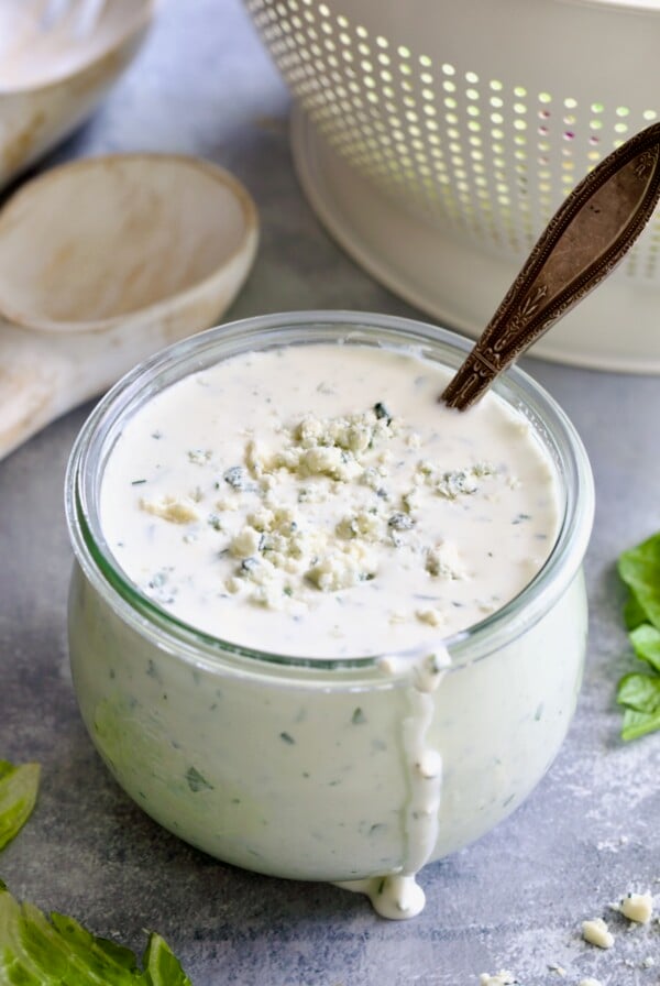 Best Blue Cheese Dressing Recipe in glass jar with spoon and colander in the background.