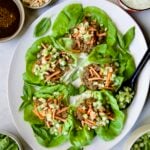 Vietnamese Beef Lettuce Wraps on oval white platter with lime wedges and accompaniments around it.