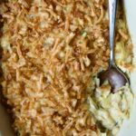 Creamed Cabbage Casserole in white oval baking dish with ornate serving spoon.