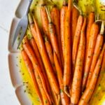 Hot Honey Roasted Carrots on white oval platter with serving fork garnished with fresh parsley.
