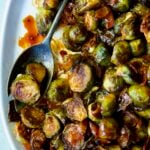 Maple Bacon Gochujang Brussels Sprouts on white platter with serving fork.