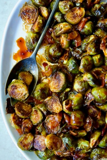 Maple Bacon Gochujang Brussels Sprouts on white platter with serving fork.