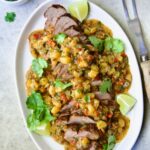 Sliced and sauced Caribbean Pork Tenderloin on white oval platter garnished with cilantro and lime wedges.
