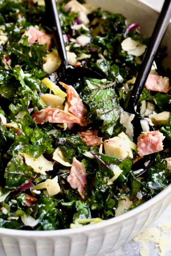 Chopped Kale Salad in round white bowl with black utensils scooping some up.