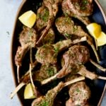Greek Lamb Chops on black oval platter garnished with lemon wedges.