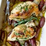 Two Roast Split Chicken Breasts with Potatoes and Shallots in white rectangular baking dish.