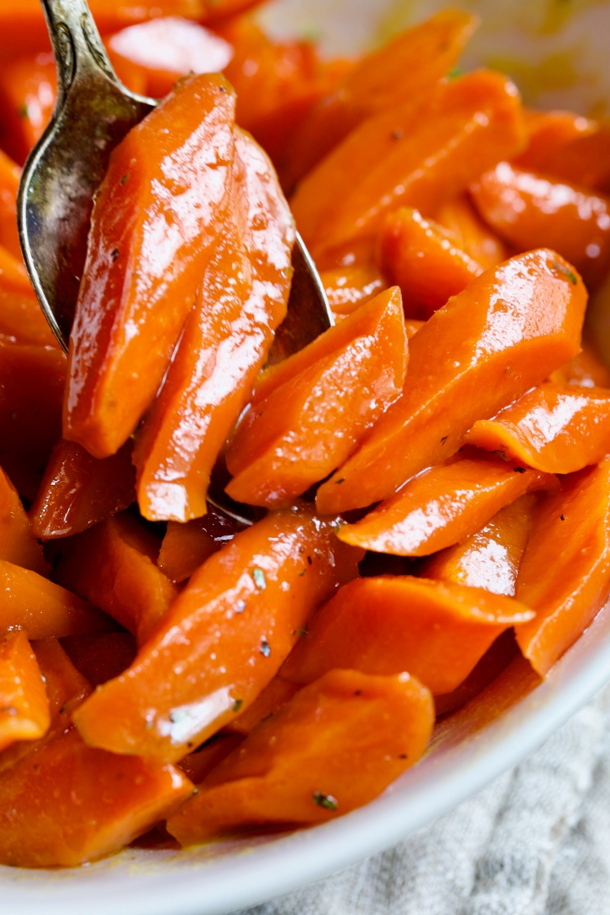 Bourbon-Glazed Carrots being spooned into white bowl.