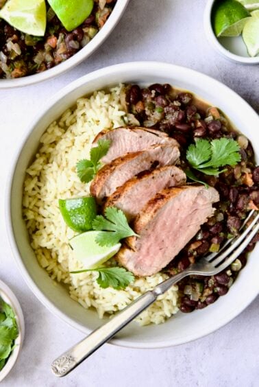 Four slices of Cuban-Style Pork Tenderloin with Black Beans and rice in white bowl.