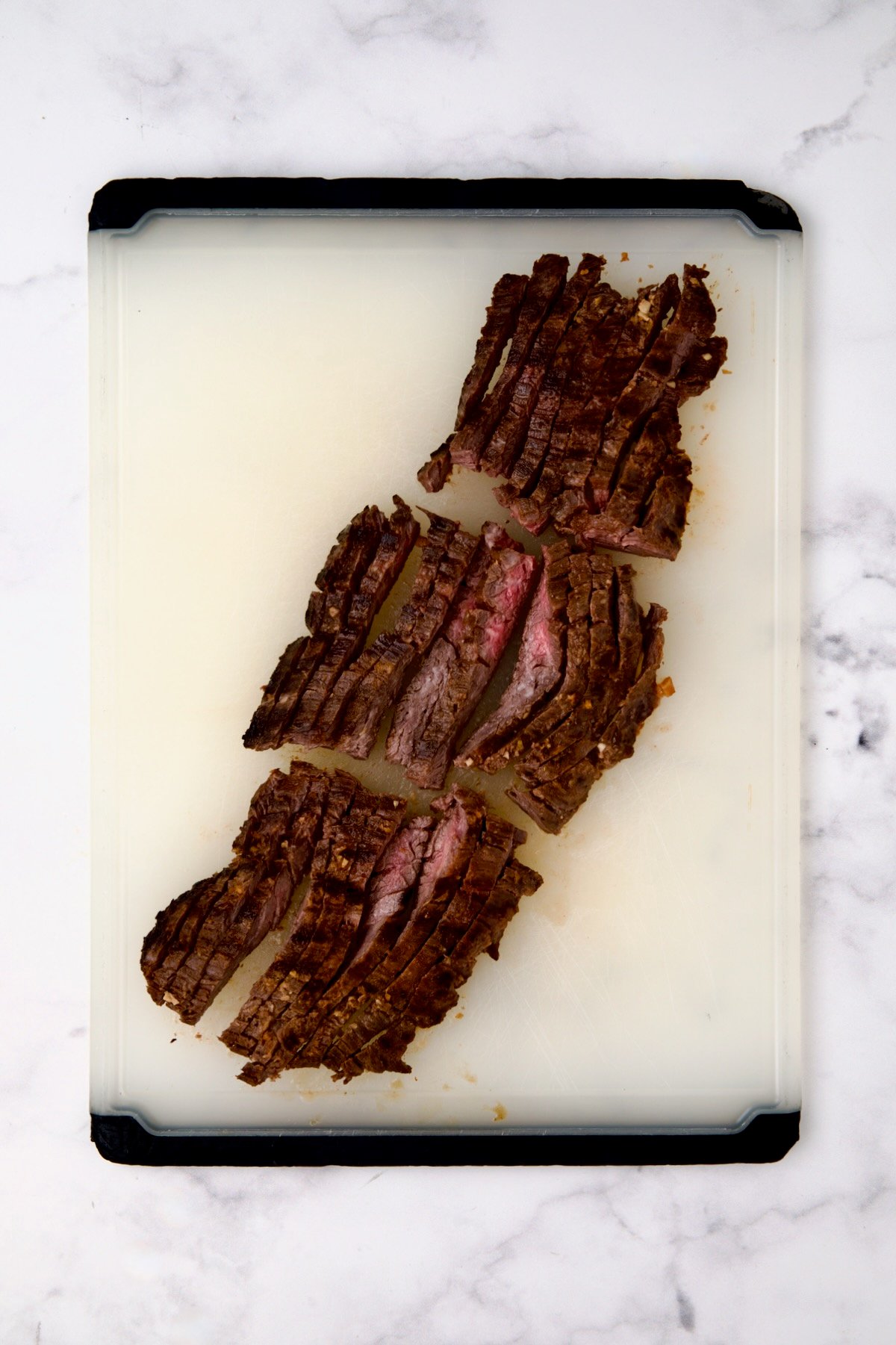 Grilled skirt steak on a white plastic cutting board after being sliced.