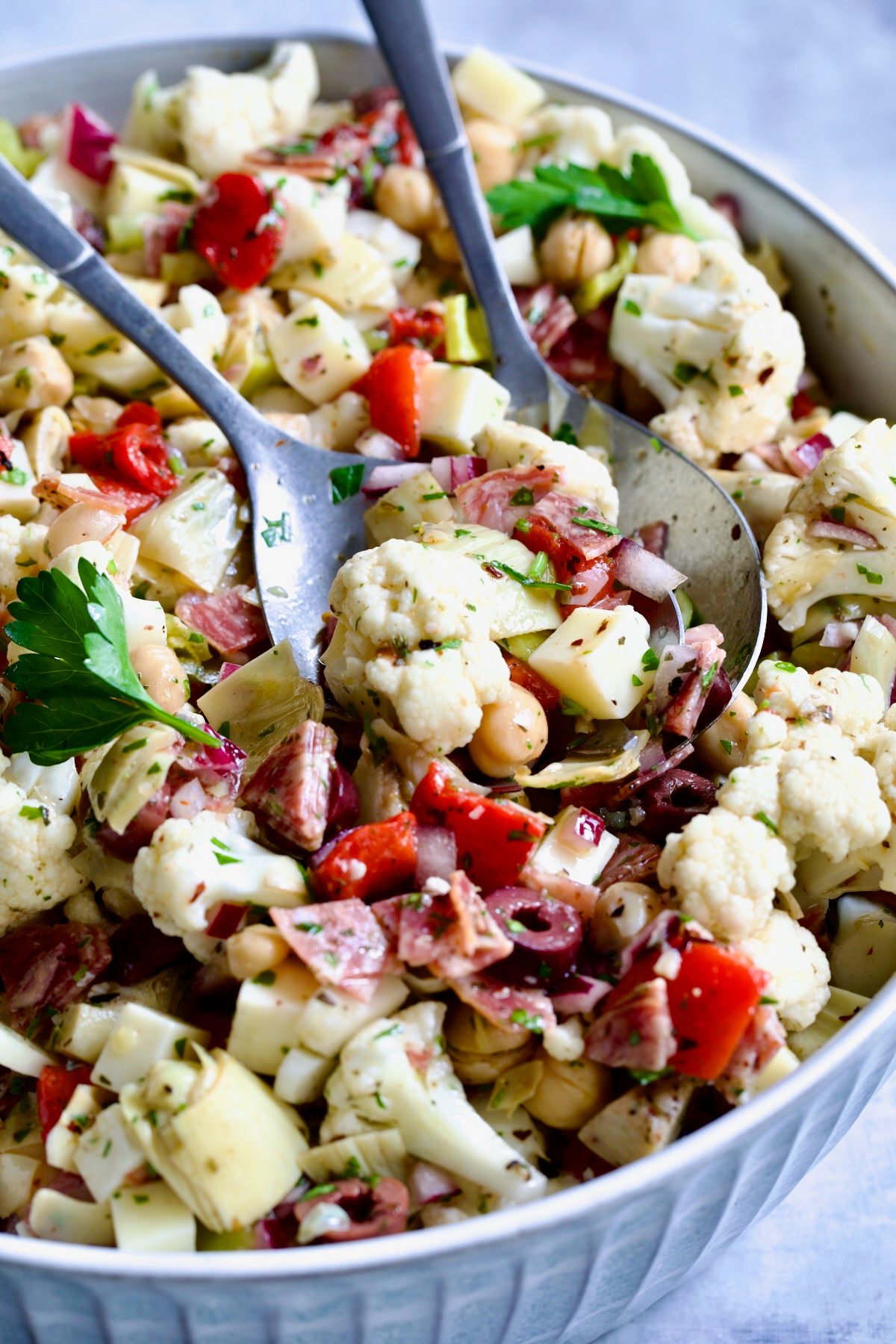 Cauliflower Antipasto Salad in blue serving bowl with serving utensils.