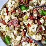 Cauliflower Antipasto Salad in serving bowl with serving utensils.