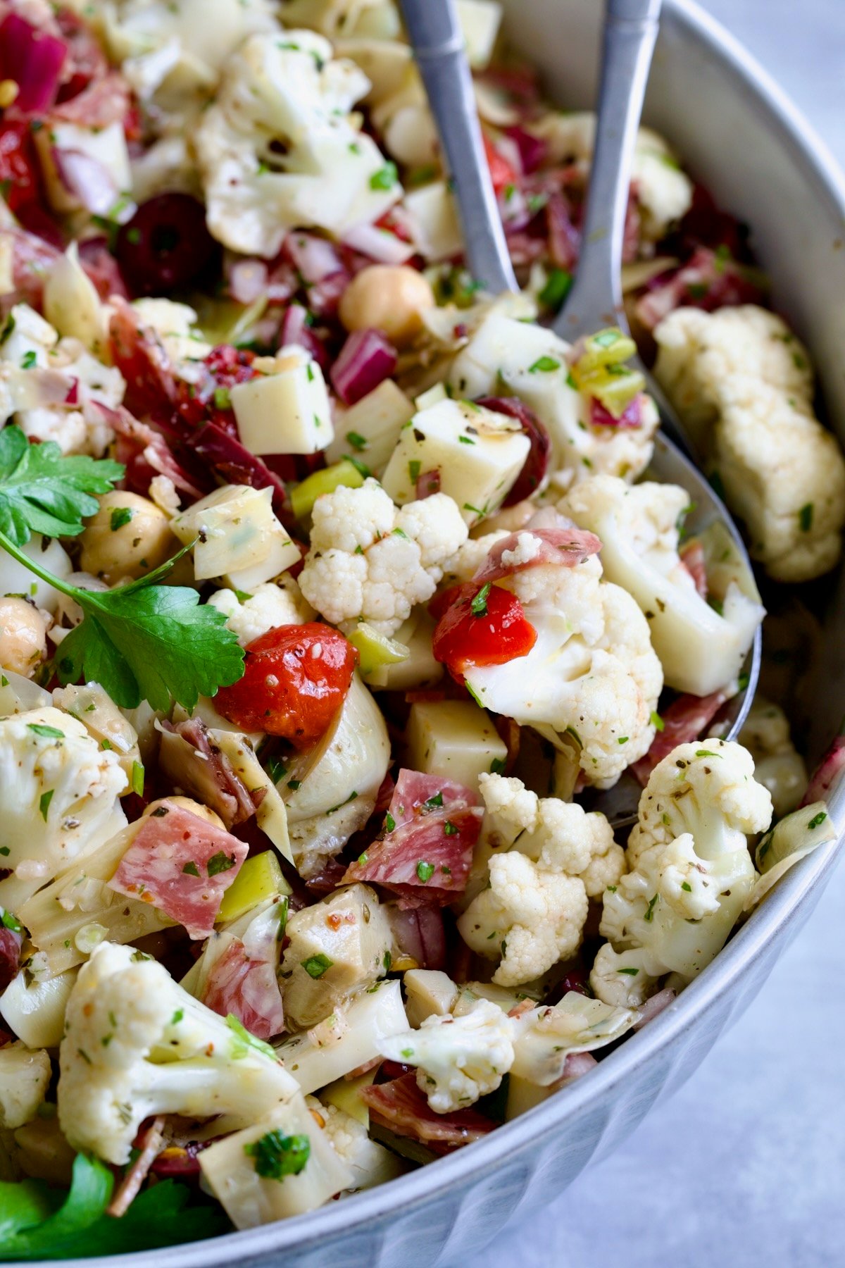 Cauliflower Antipasto Salad in blue serving bowl with serving utensils.