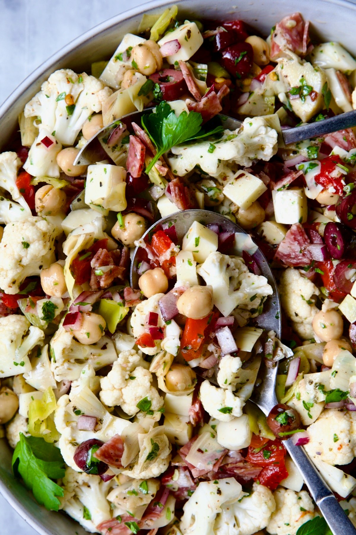 Cauliflower Antipasto Salad in serving bowl with serving utensils.