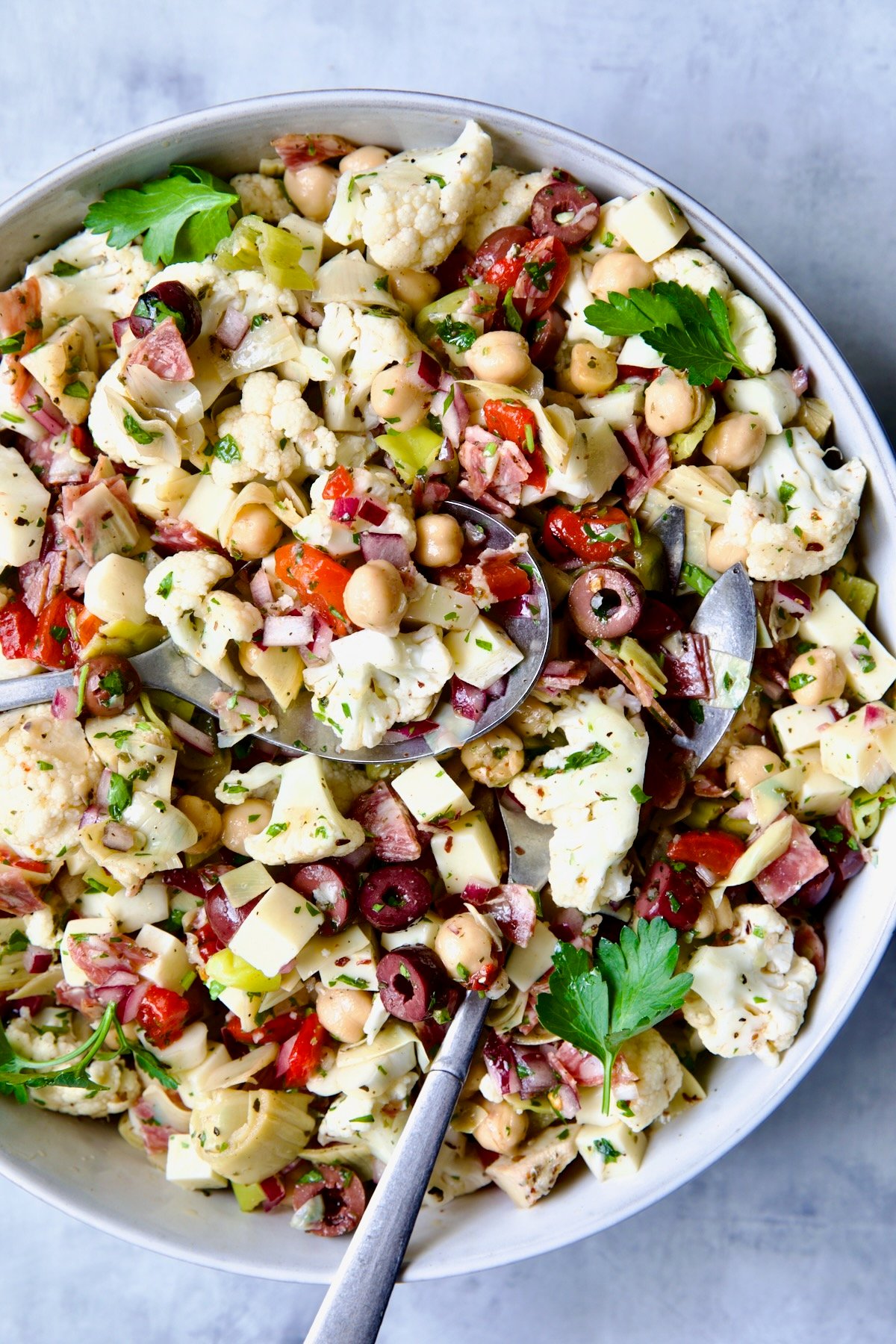 Cauliflower Antipasto Salad in blue serving bowl with serving utensils.