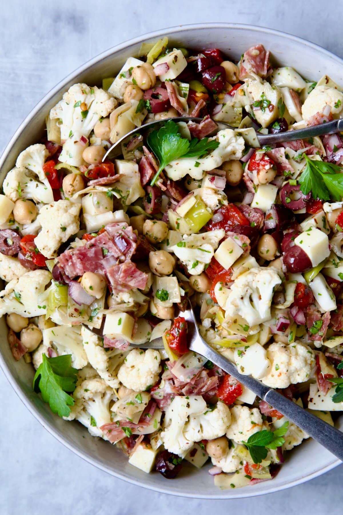 Cauliflower Antipasto Salad in serving bowl with serving utensils.