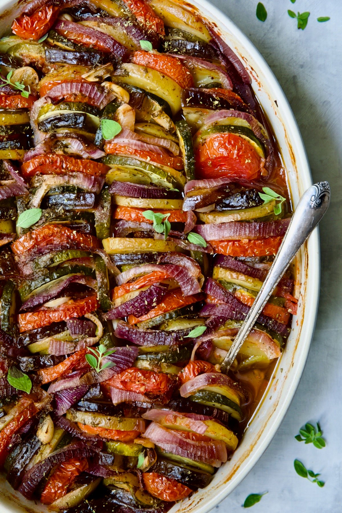 Briam (Greek Roast Vegetables) in oval white gratin dish with serving spoon.