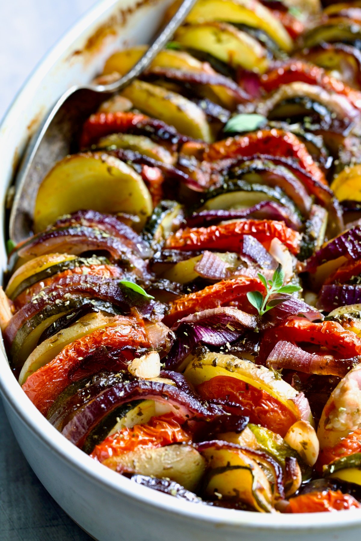 Briam (Greek Roast Vegetables) in oval white gratin dish with serving spoon.