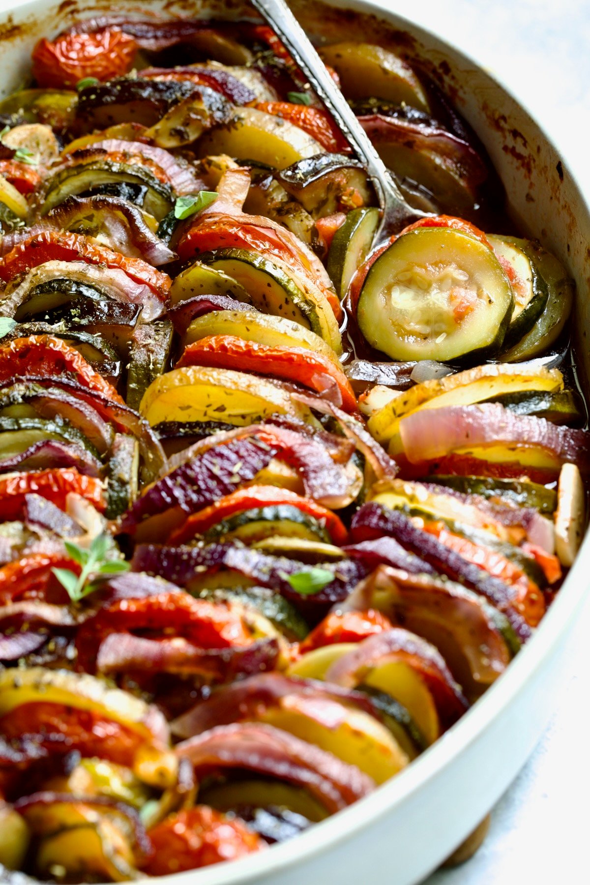 Briam (Greek Roast Vegetables) in oval white gratin dish with serving spoon.