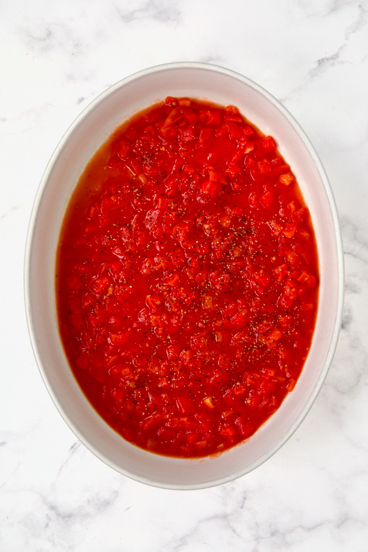 Petite diced tomatoes spread over the bottom of an oval white baking dish.