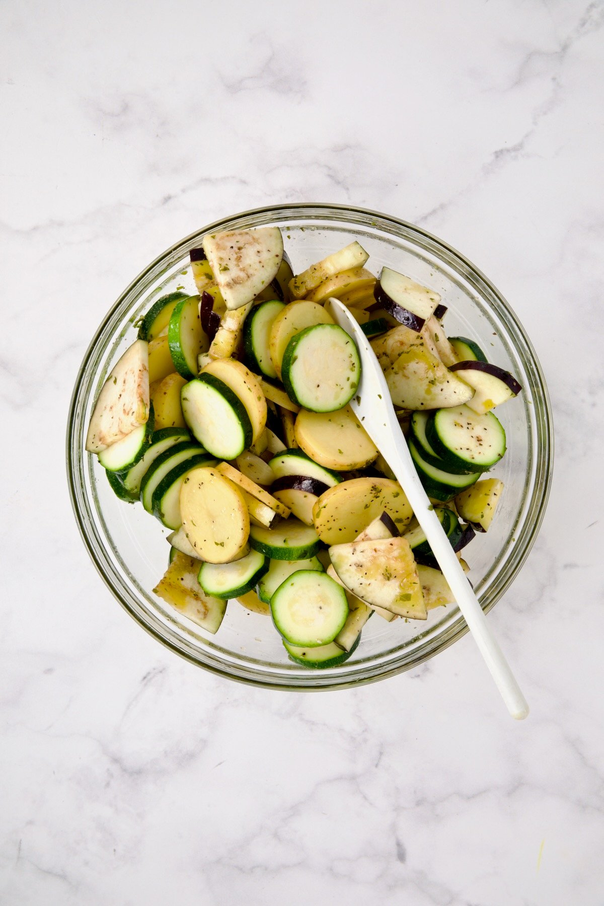 Zucchini, potatoes and eggplant being tossed with flavored olive oil and dried oregano.