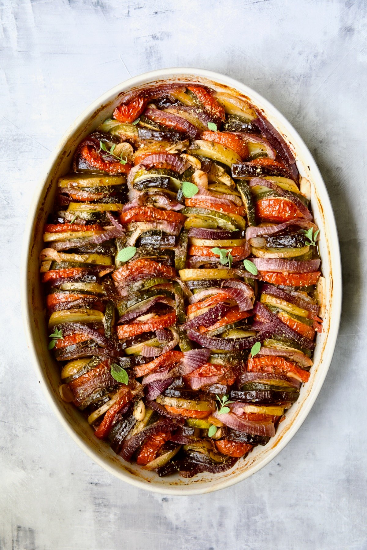 Briam (Greek Roast Vegetables) in oval white gratin dish with serving spoon.