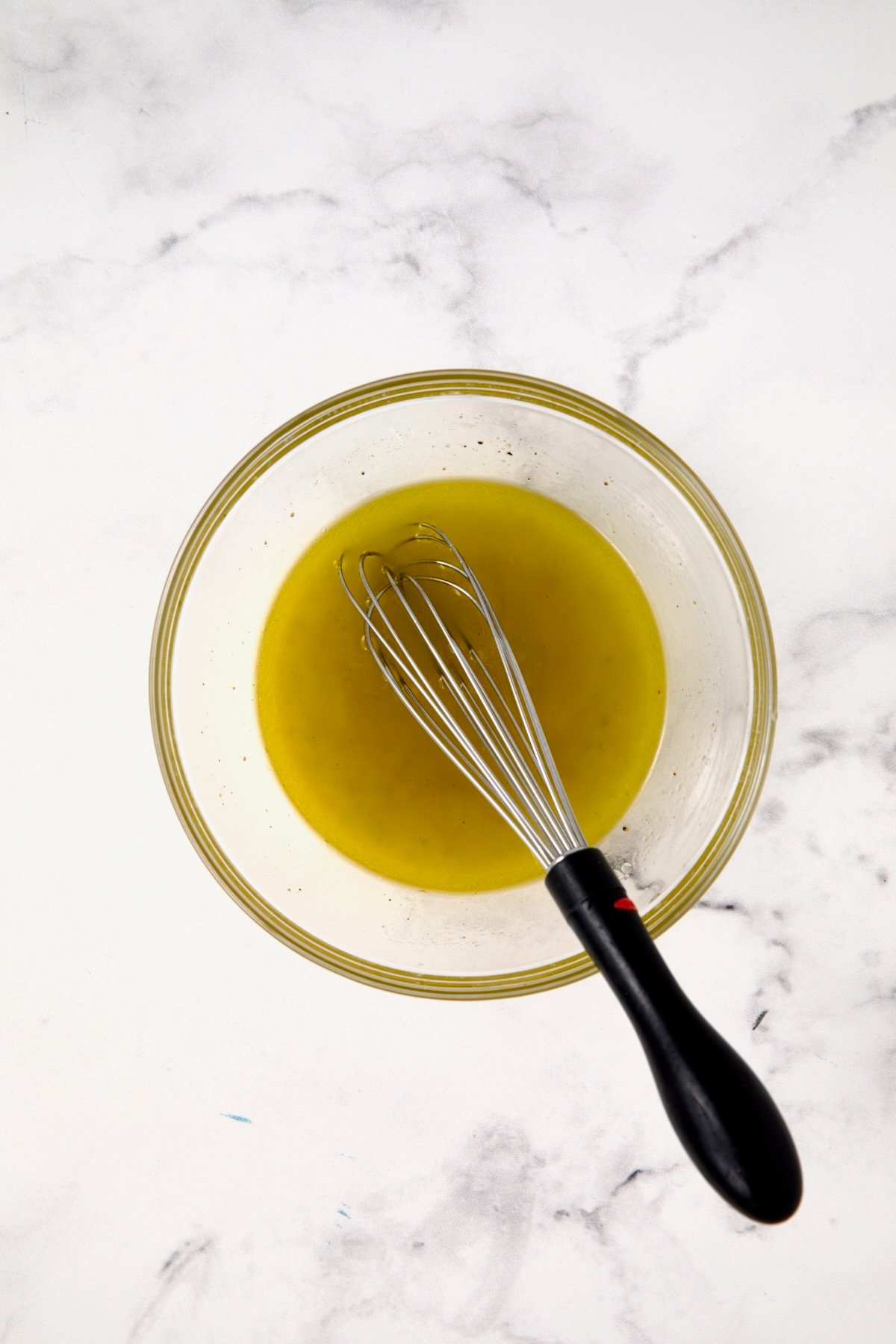 Lemon vinaigrette in glass bowl with black-handled whisk.